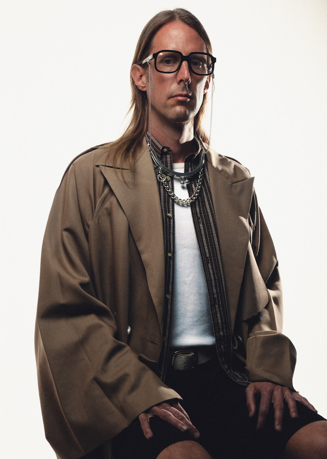 Alex wears glasses and accessories by Huma Eyewear, trench by Setchu, shirt and belt stylist’s own, tank top by Grifoni and trousers by JordanLuca.
